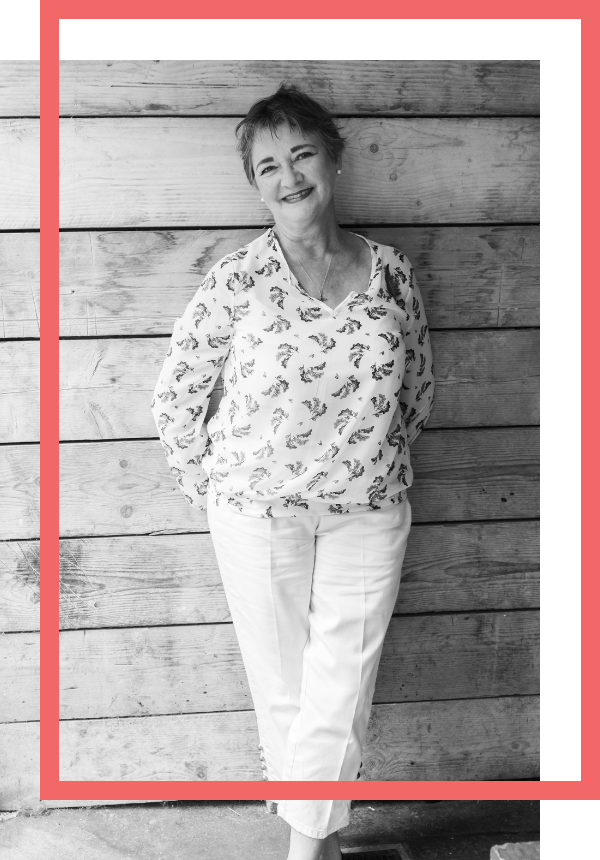 Mary against wooden background Black and white photograph of Mary Wardell, a copywriter in East Cornwall, standing against a wood -panelled wall. The image has an offset red border.